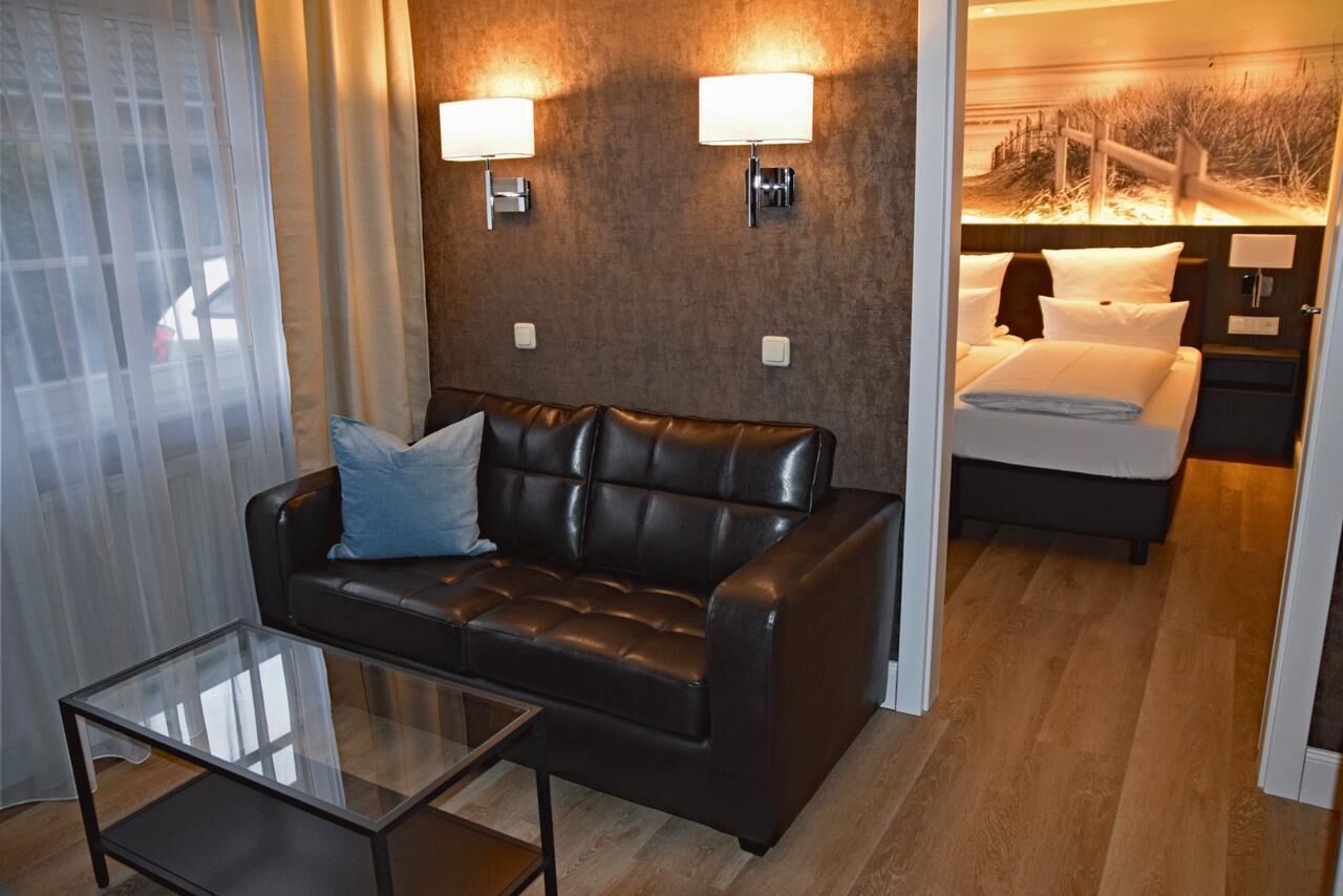 A hotel room with a leather sofa, a glass coffee table, and a bed with white bedding.