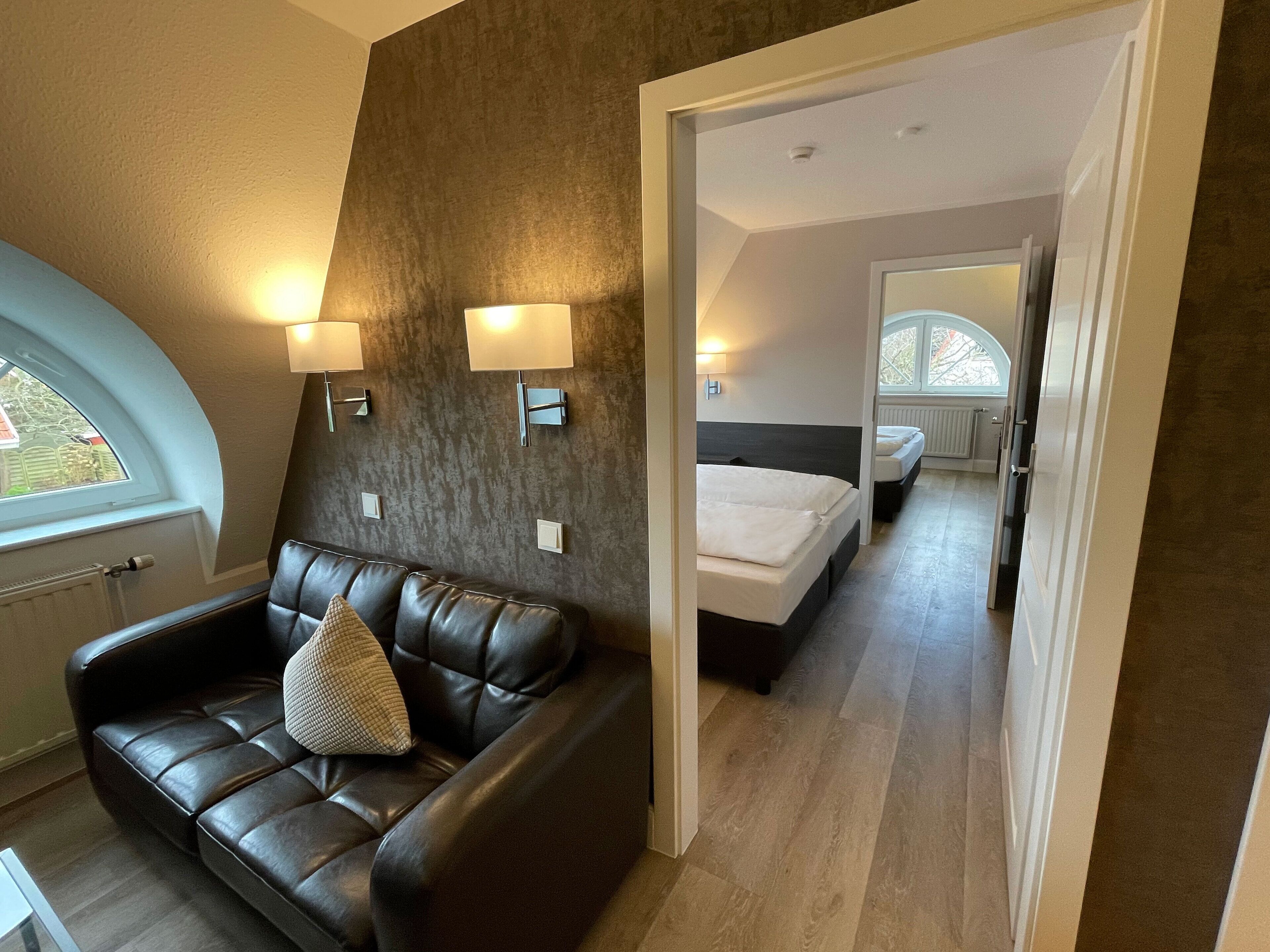 Un dormitorio moderno con una cama grande, un sofá de cuero y dos lámparas de pared.