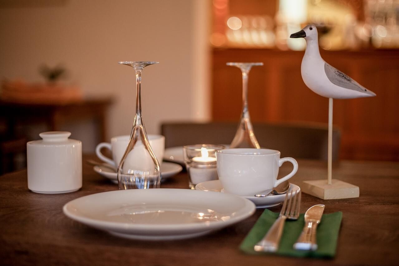 Una mesa de comedor con platos blancos, una copa, una tetera, una taza y un candelabro con forma de pájaro.