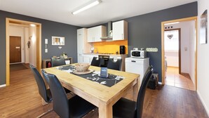 A compact kitchen with modern appliances, a dining area with a wooden table and chairs, and a small refrigerator.