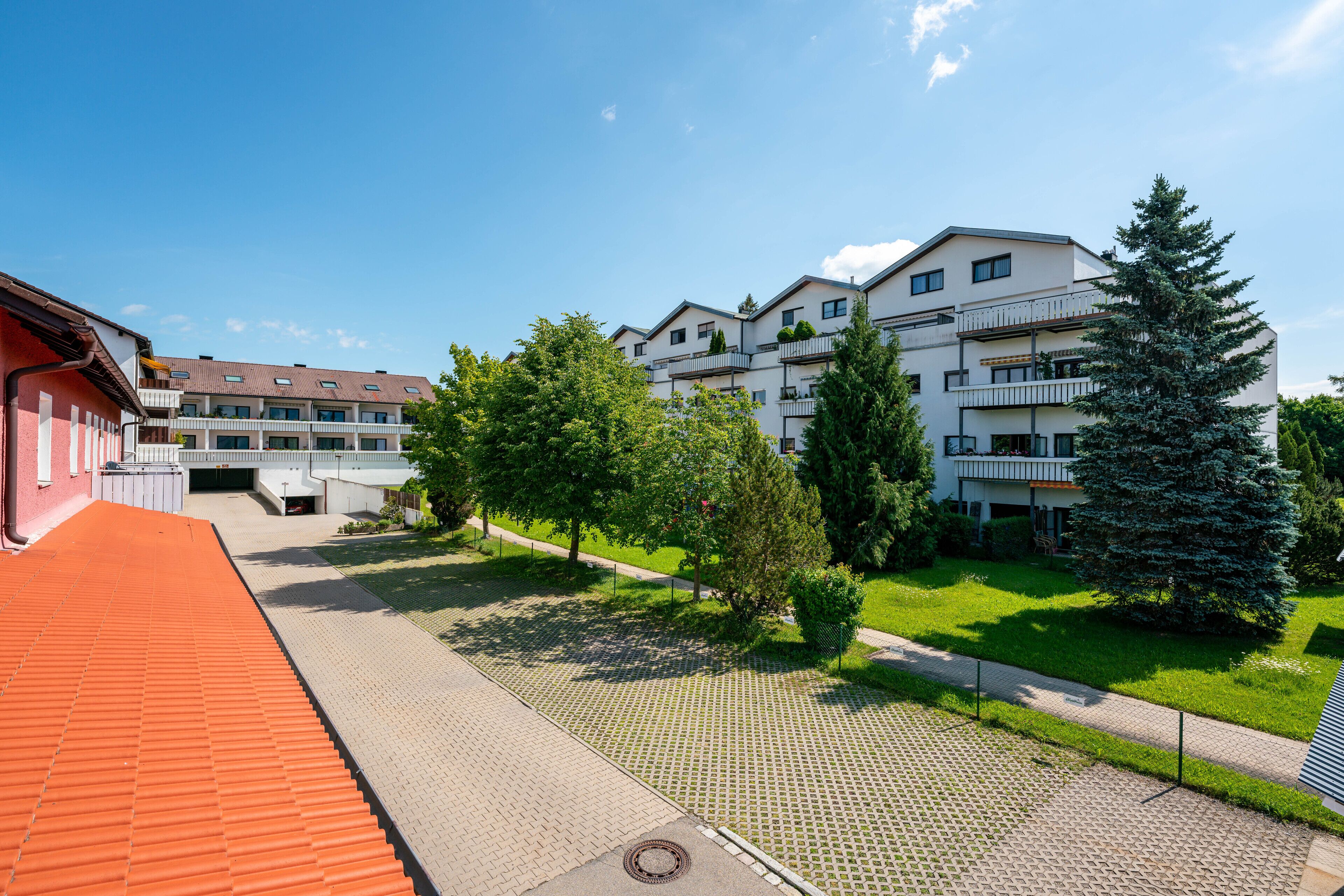 Un immeuble résidentiel doté de nombreux balcons, d’une cour pavée et entouré de verdure.
