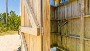 Una struttura in legno con una porta aperta che mostra un angolo doccia, con tubature e una finestra sopra.