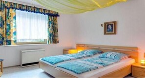 Double bed with a wooden headboard and two bedside tables, each with a lamp, and a window with a curtain.