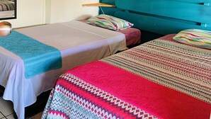 Une chambre avec deux lits, un mur de couleur turquoise, un ventilateur et un petit tableau.