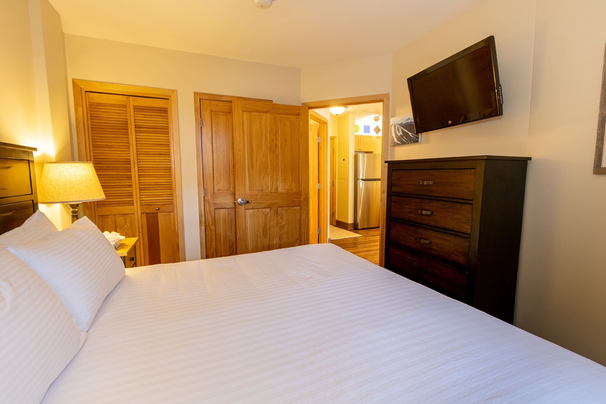 Ein Hotelzimmer mit einem Bett, einem an der Wand befestigten Fernseher, Holztüren und einem Schminktisch.