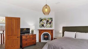 Una camera da letto con un letto, una cassettiera in legno, una televisione, un camino e un quadro appeso al muro.