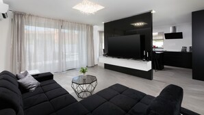 A modern living room with a large flat-screen TV, black sofas, a glass coffee table, and a kitchen area in the background. - VILLA ELLA - Pool villa for 8 persons near Medulin (Medulin)