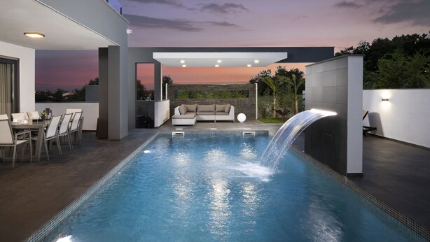 A modern outdoor pool area with a waterfall feature, a dining area with chairs and a table, and a sofa. - VILLA ELLA - Pool villa for 8 persons near Medulin (Medulin)