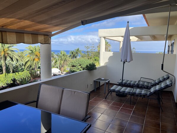 Ein Balkon mit Meerblick, ein Tisch, Stühle und ein kleiner Tisch mit einer Lampe.
