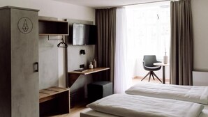 Habitación de hotel con dos camas, un escritorio con silla, un televisor montado en la pared y una ventana con cortinas.