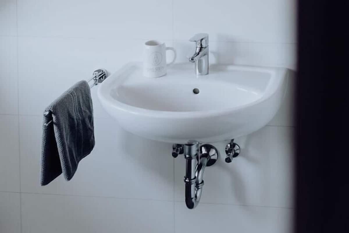 Un baño con un lavamanos blanco, una toalla y un espejo redondo en la pared.