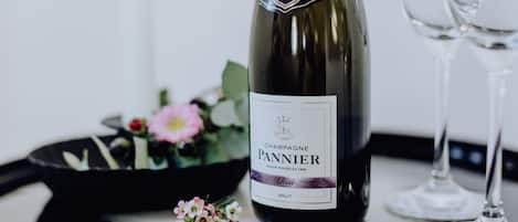 A bottle of champagne with a label, two wine glasses, and a small flower arrangement on a reflective surface.