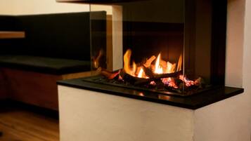 A modern fireplace with a glass front, set in a minimalist room with a wooden floor and a dark-colored bench.