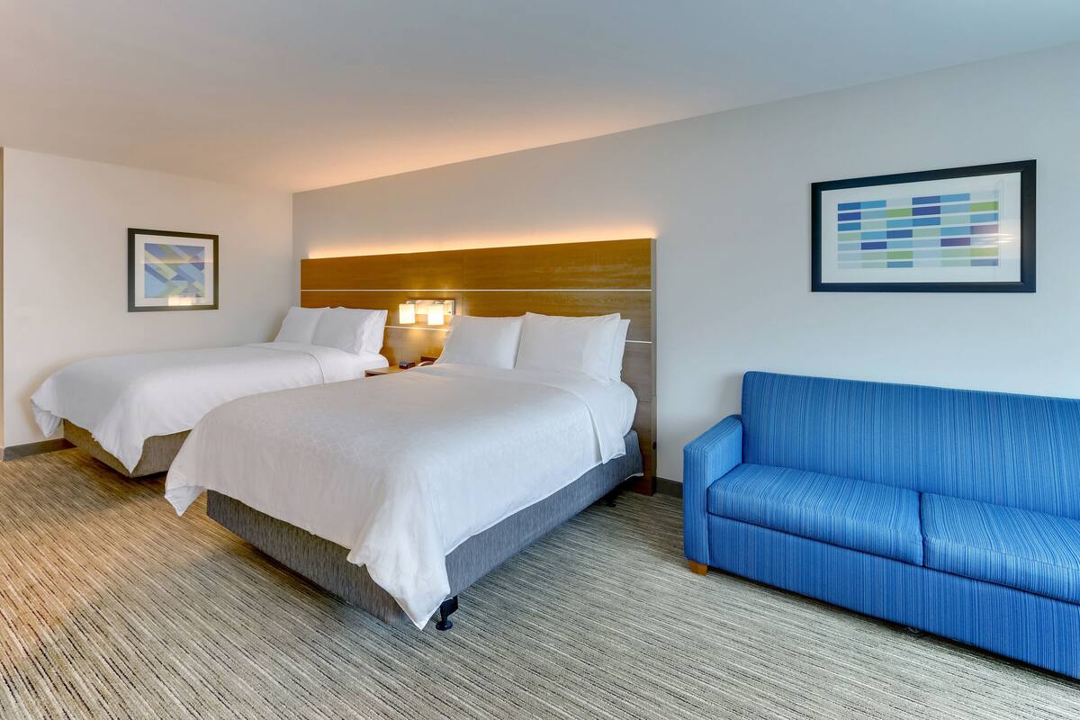 A hotel room with two beds, a blue sofa, and a wooden headboard.