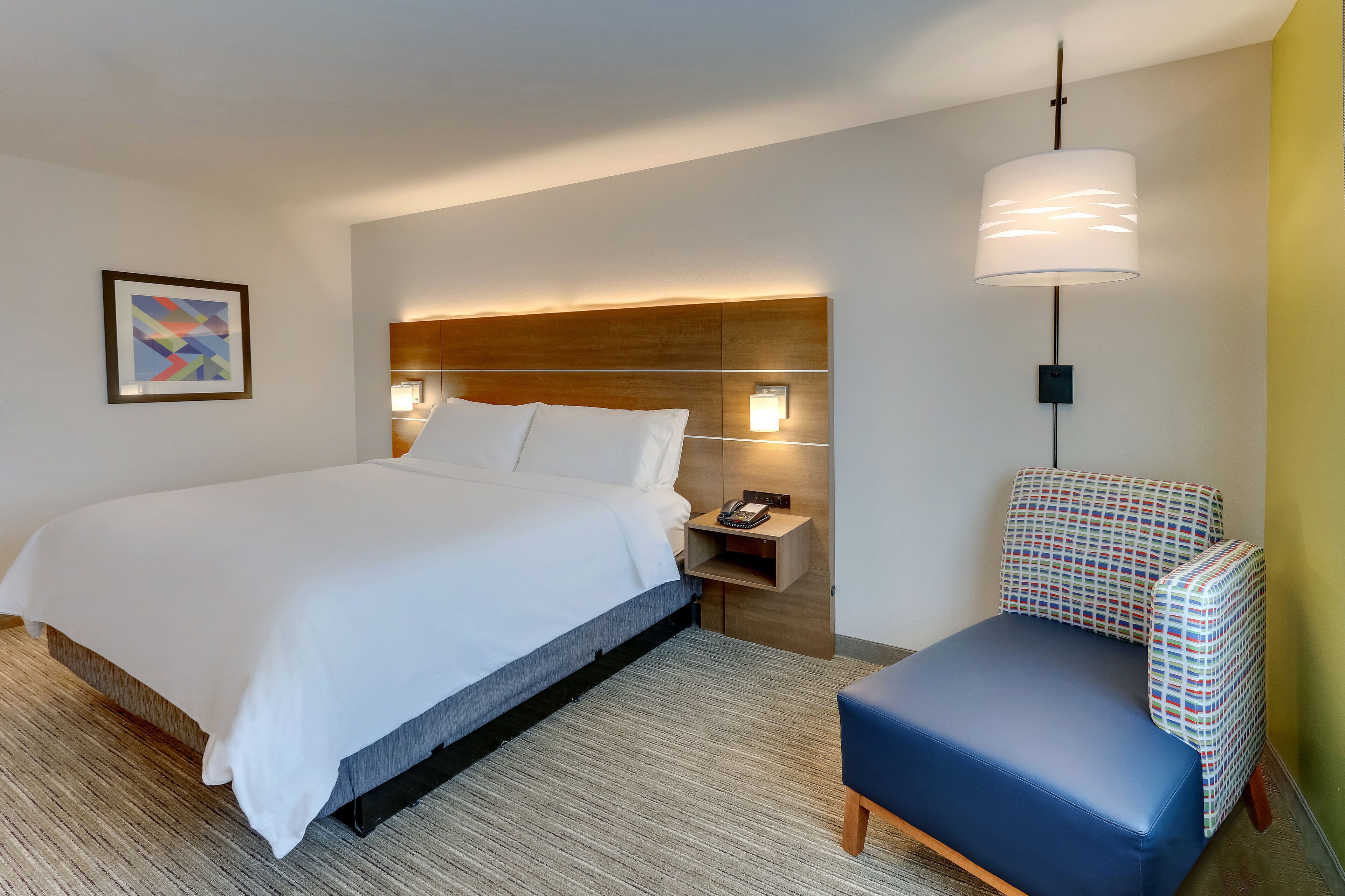 Une chambre d’hôtel avec un grand lit, une table de chevet avec une lampe, une chaise et un téléphone fixé au mur.
