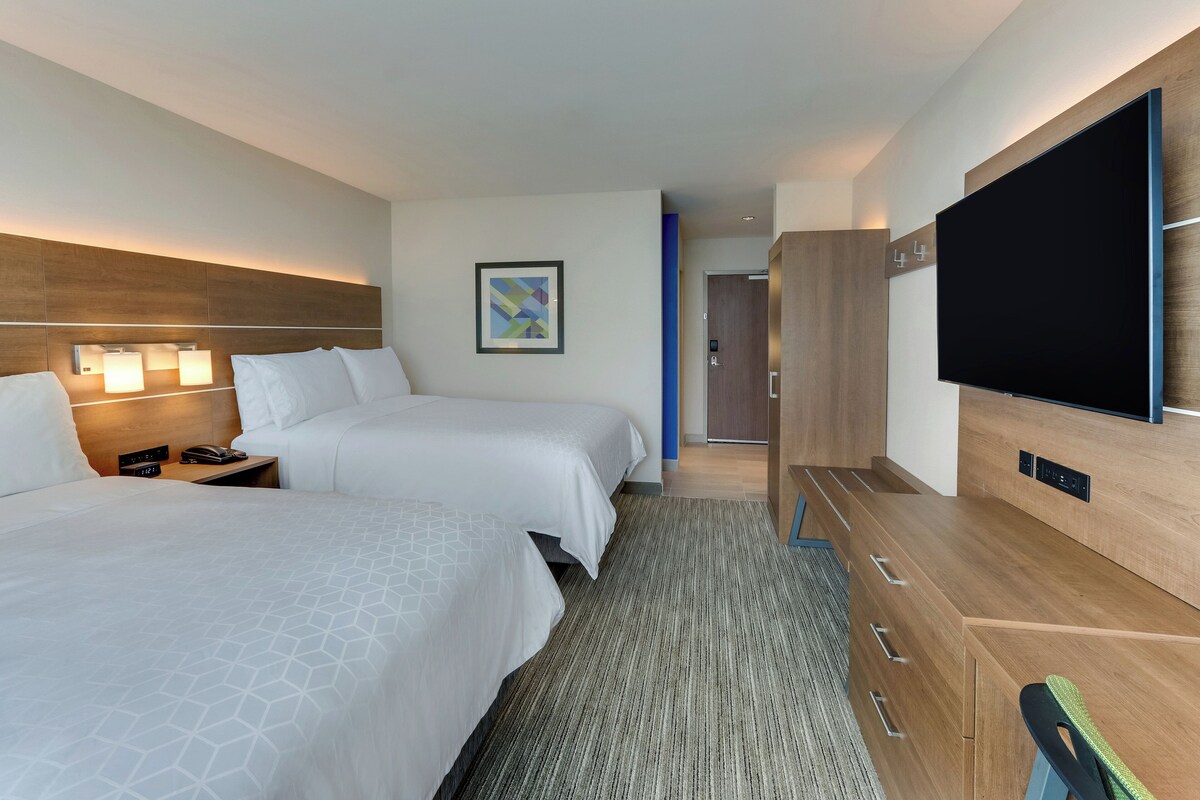 A hotel room with two beds, a flat-screen TV, a wooden dresser, and a framed picture on the wall.