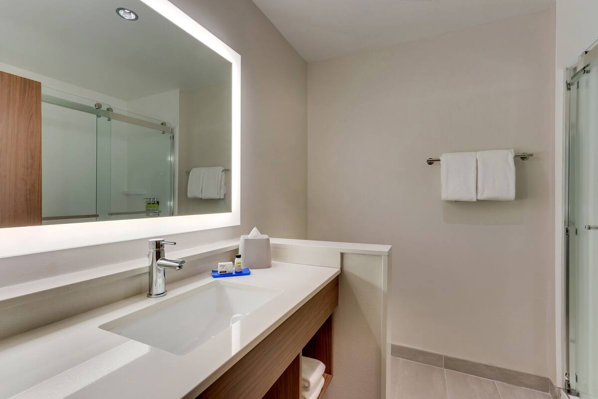 A modern bathroom with a large mirror, a white sink, and a glass shower enclosure.