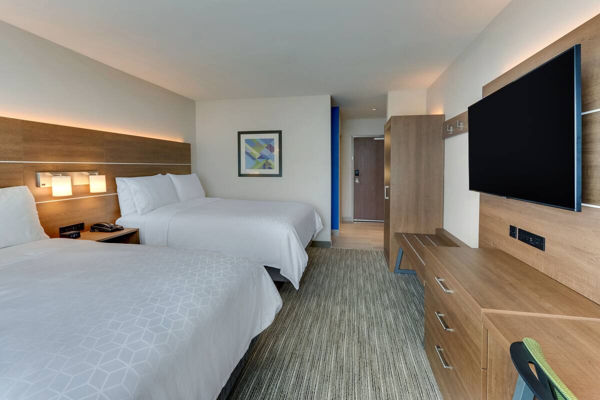 A hotel room with two beds, a flat-screen TV, a wooden dresser, and a framed picture on the wall.