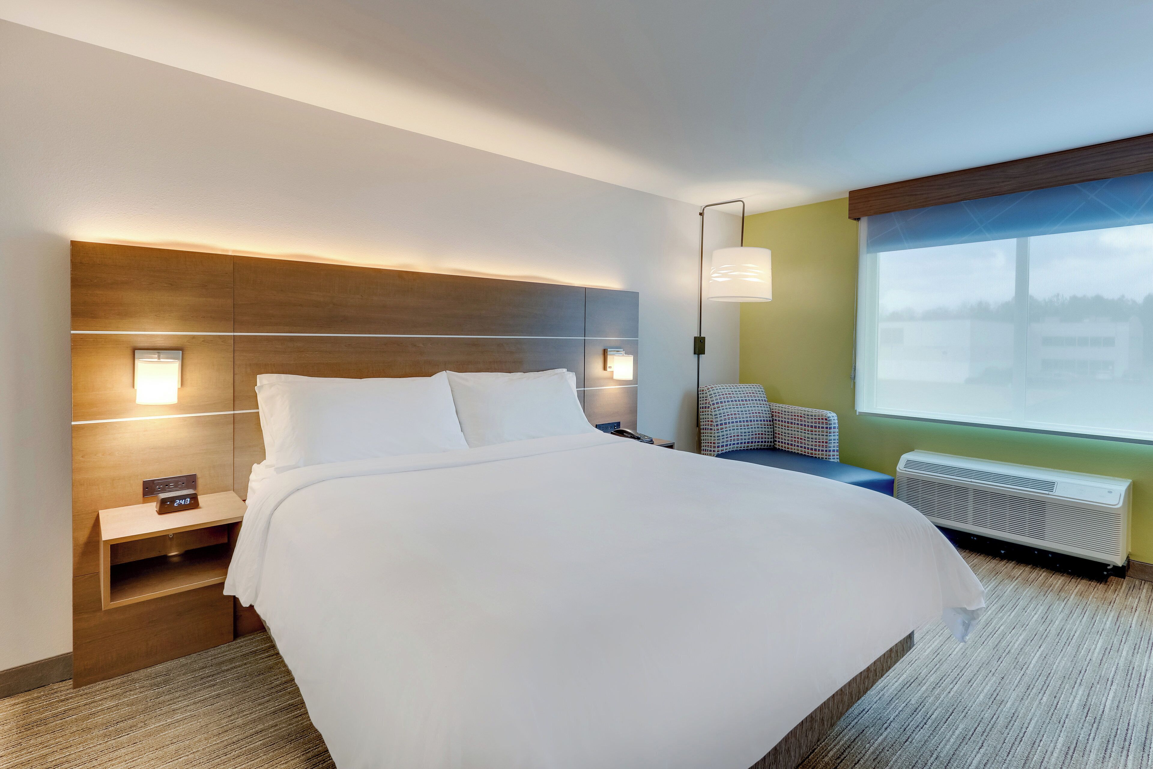 Habitación de hotel con una cama grande, mesitas de noche, una lámpara de pared, ventana con vistas y calefacción integrada.