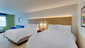 Habitación de hotel con dos camas, una mesita de noche con lámpara, una silla azul y una ventana con vistas.
