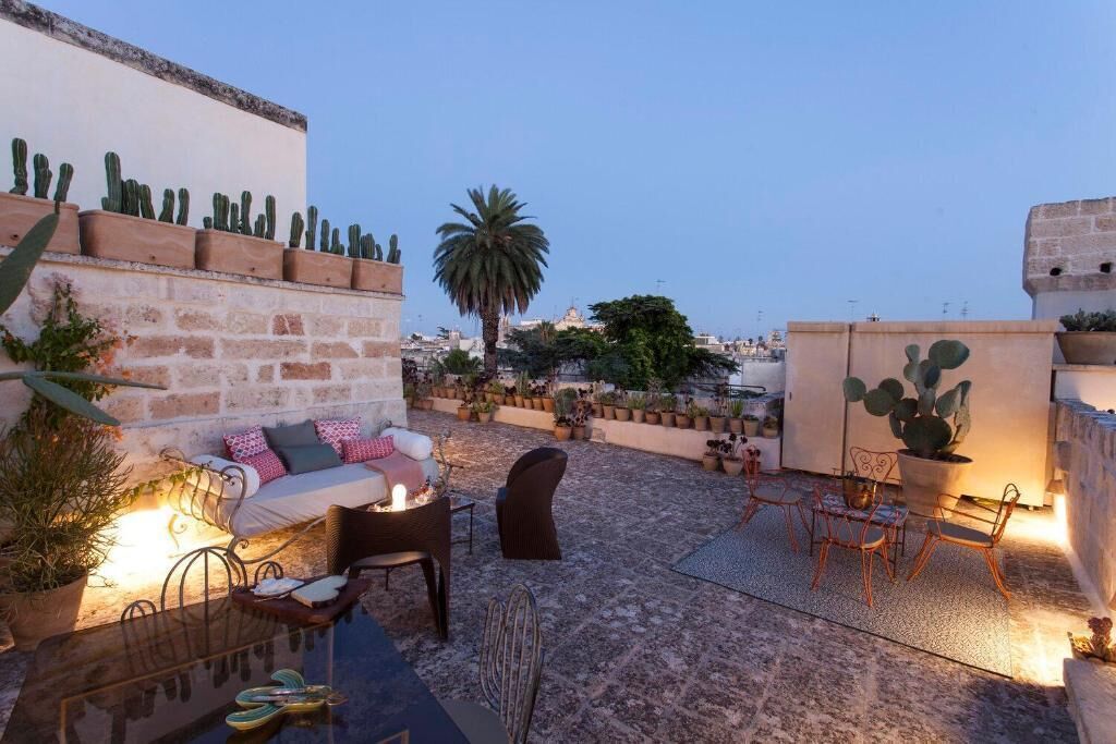 A rooftop patio with a stone floor, outdoor seating, cacti, and a palm tree.