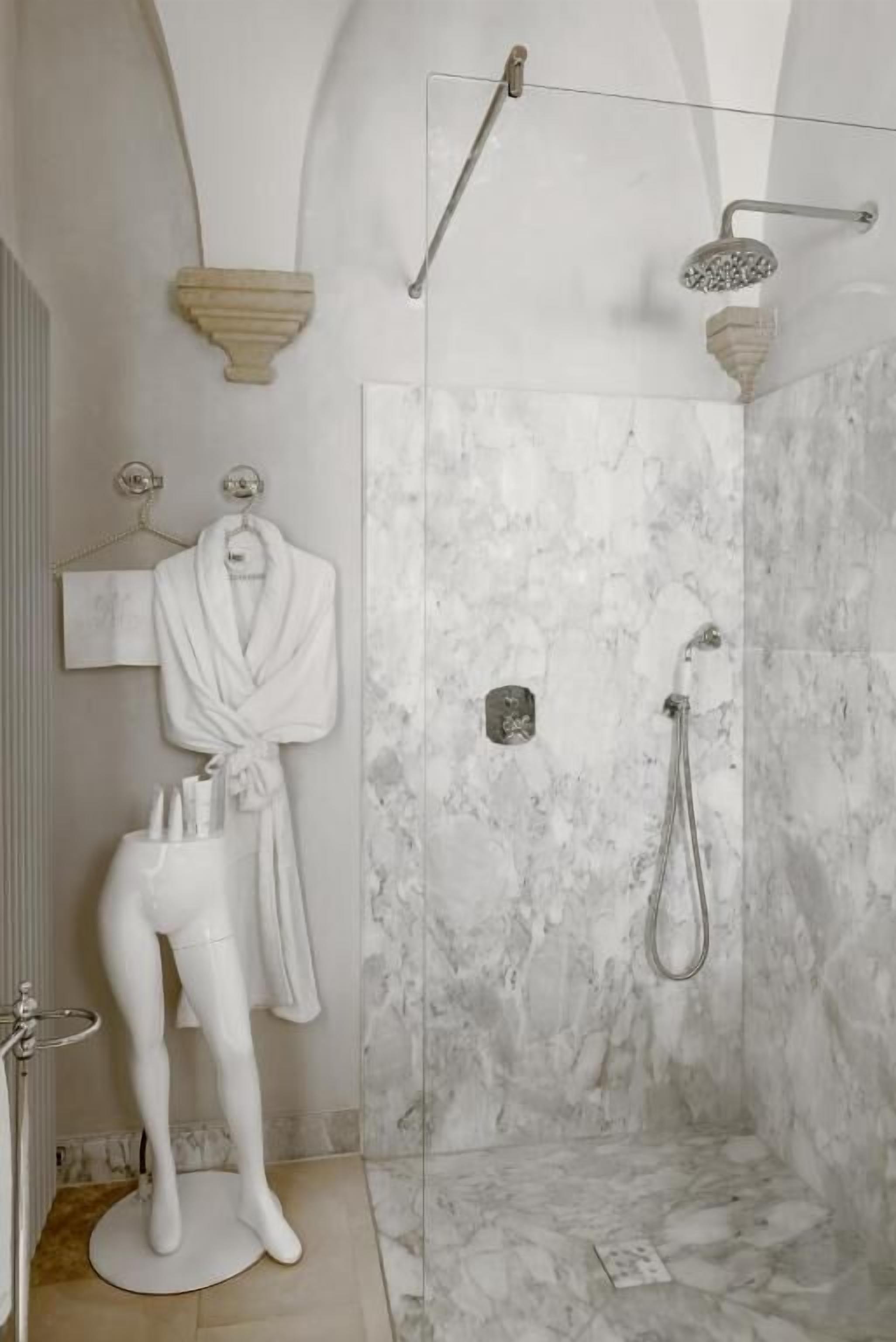 A modern bathroom with a marble shower wall, a towel rack with a robe, and a showerhead.