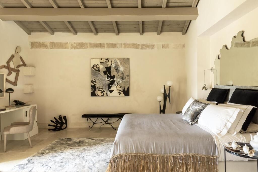 A bedroom with a bed, bedside table, desk, chair, and a wall-mounted artwork.