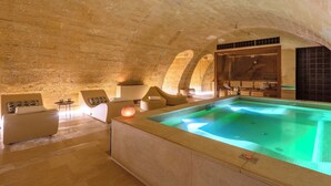 An indoor swimming pool with a stone ceiling and a spa area with seating and a massage chair. - Palazzo Maresgallo (Lecce)