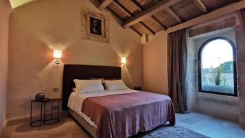 A bedroom with a bed, two bedside lamps, a small table, a rug, and a window with a view.