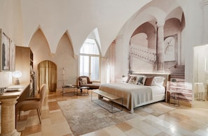 A spacious bedroom with a large bed, a desk, and a chair, featuring arched ceilings and a view of a staircase. - Palazzo Maresgallo (Lecce)