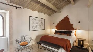 A bedroom with a bed, a bench, a chair, a framed artwork, and a unique headboard.