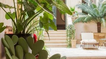 Un espacio al aire libre moderno con un área de estar y un diseño de silla único, rodeado de exuberante vegetación y una fachada de edificio clásico al fondo.