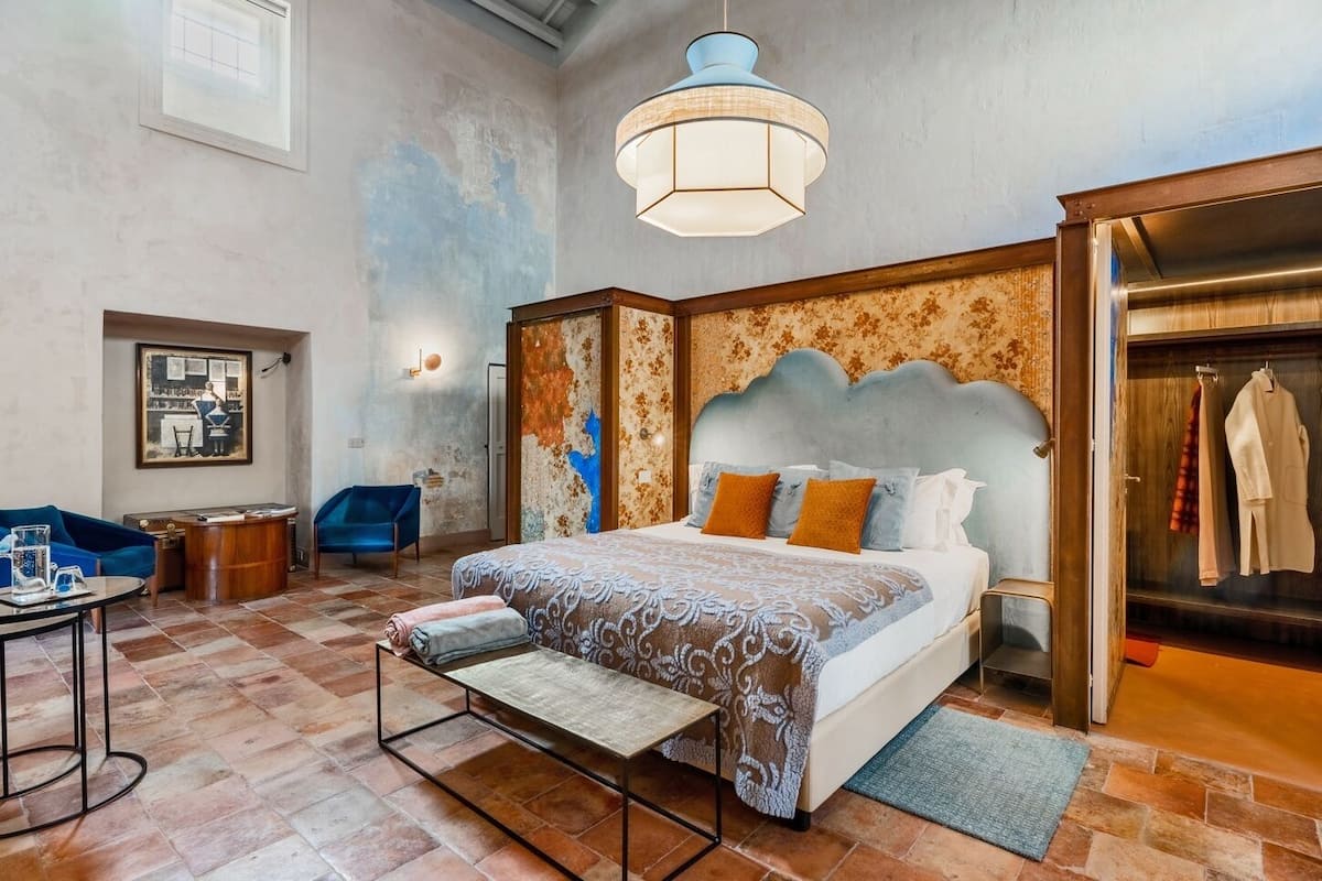 A spacious bedroom with a large bed, a desk, and a chair. There is a wardrobe and a hanging closet.