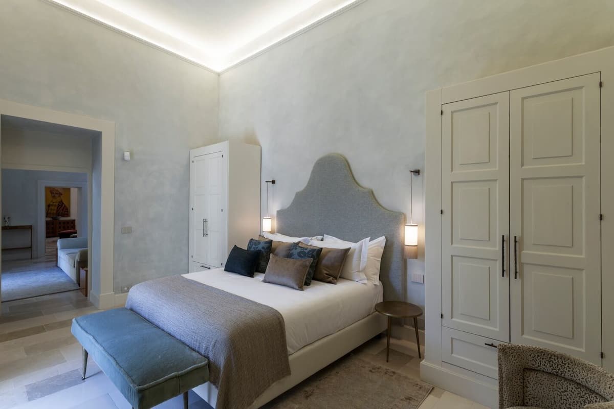 A bedroom with a large bed, bedside tables, a wardrobe, and a bench.