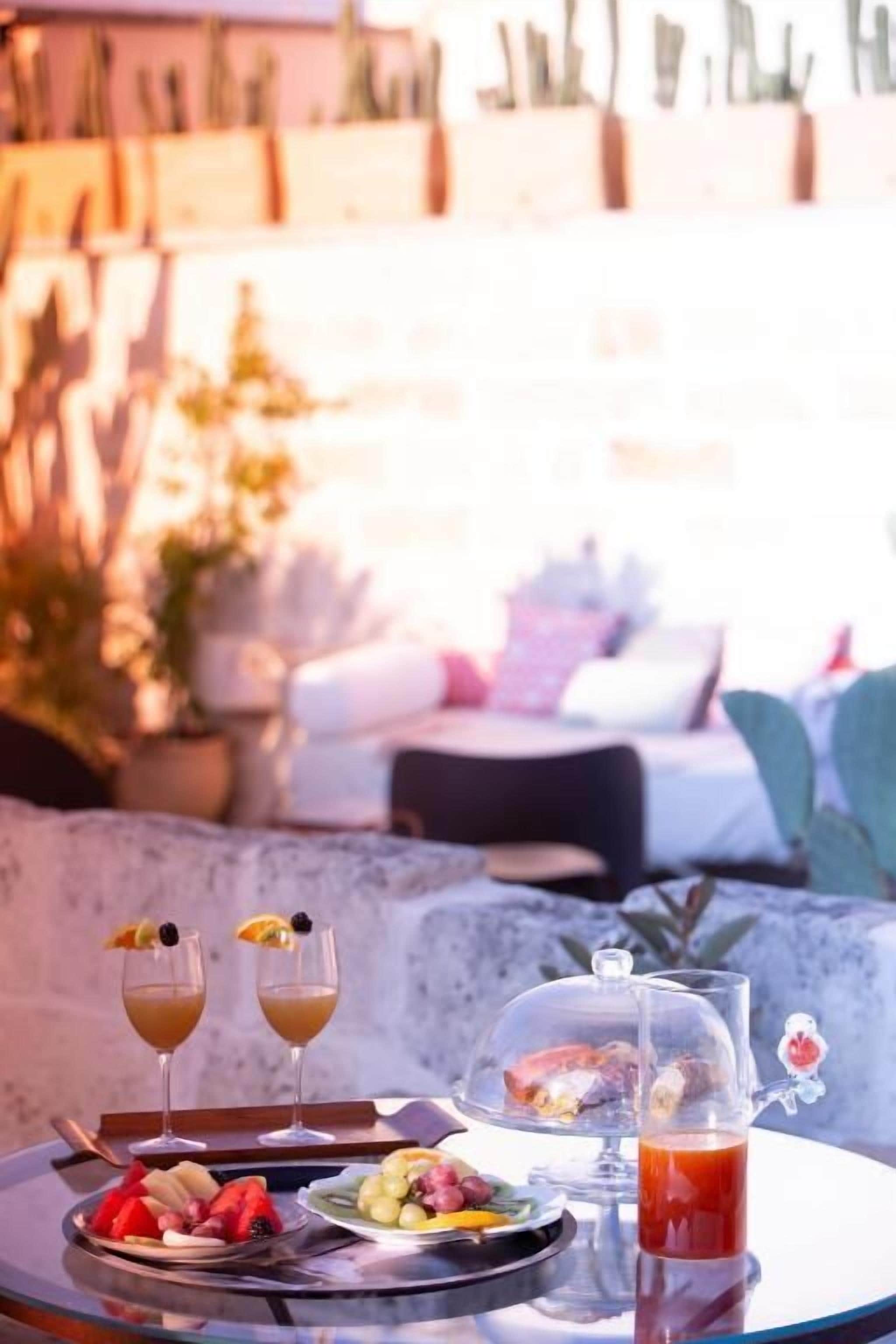 A table set with two drinks, a fruit platter, and a tea pitcher, with a cactus garden in the background.
