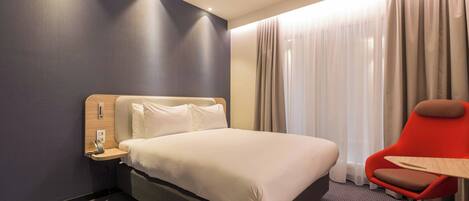 A hotel room with a bed, a desk, a chair, and curtains.
