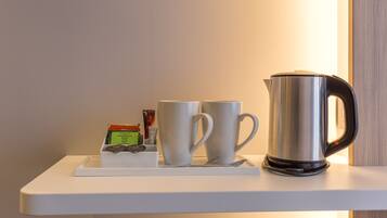A white shelf with a stainless steel kettle, two white cups, and a small box containing a tea bag and a packet.