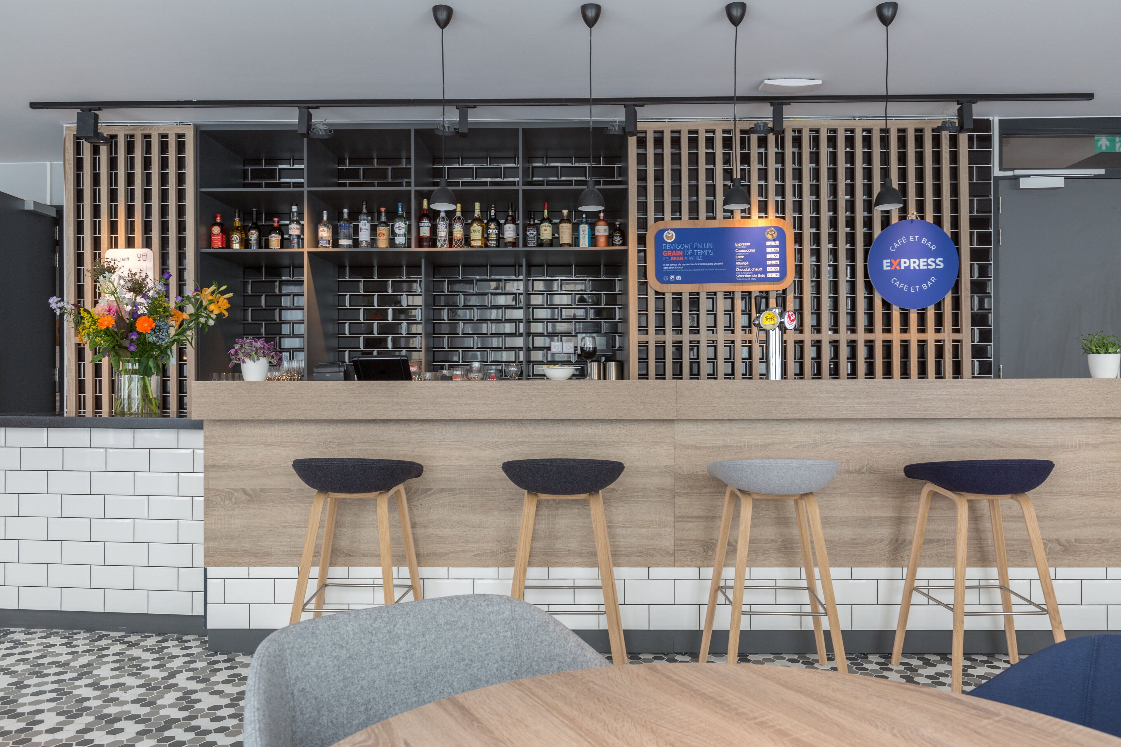 A modern bar area with a wooden counter, bar stools, and a menu board.