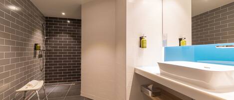 A modern bathroom with a grey and white tiled wall, a white sink with a blue countertop, and a small step stool.