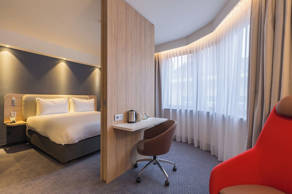 A hotel room with a bed, a desk, a chair, and a window with curtains.