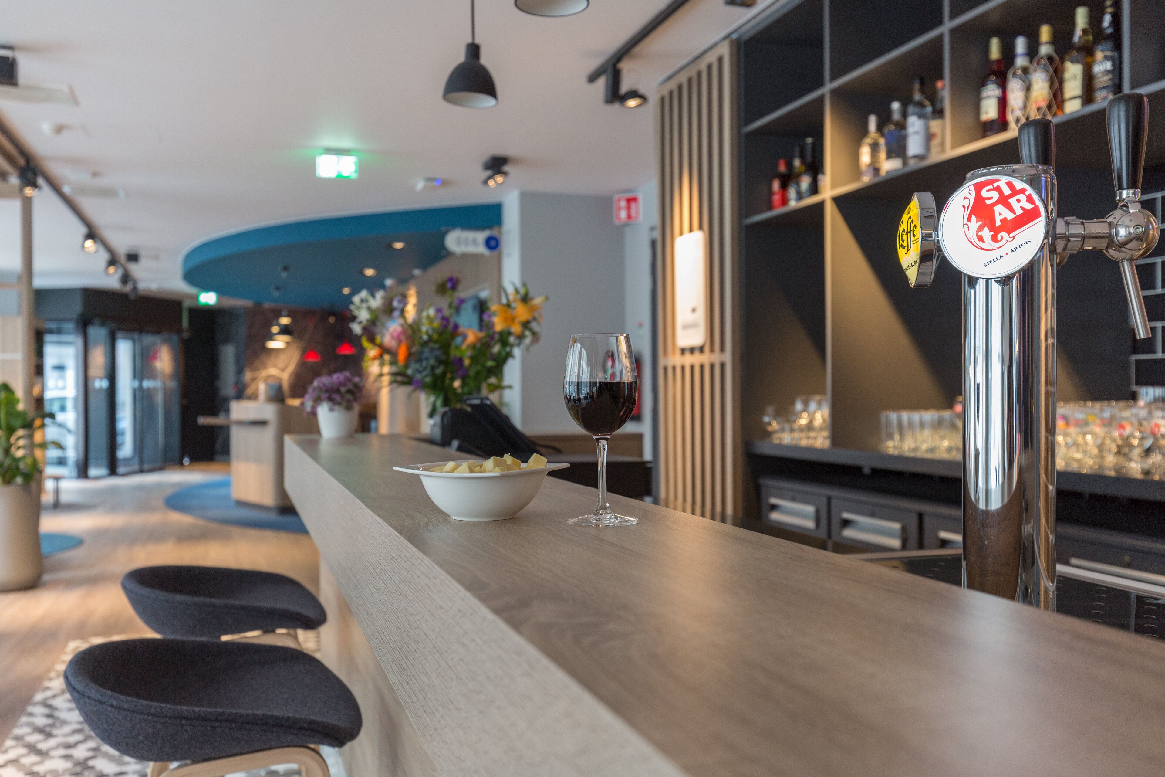 Eine Bar mit Hockstühlen, einer Schale Snacks, einem Weinglas und einem Zapfhahn mit der Aufschrift 'Stella Artois'.