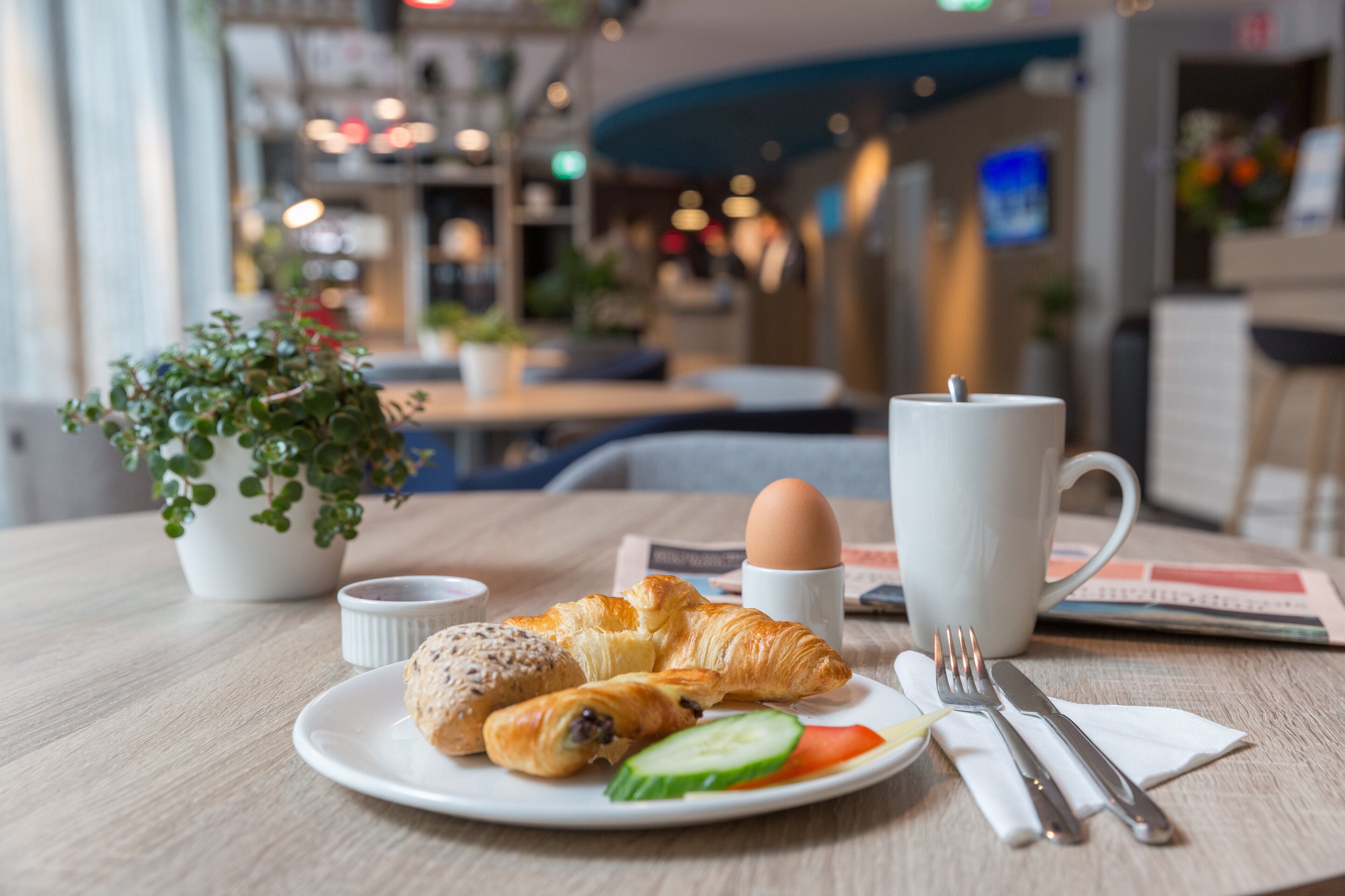 A breakfast setting with croissants, a boiled egg, a cup, and a fork on a table.