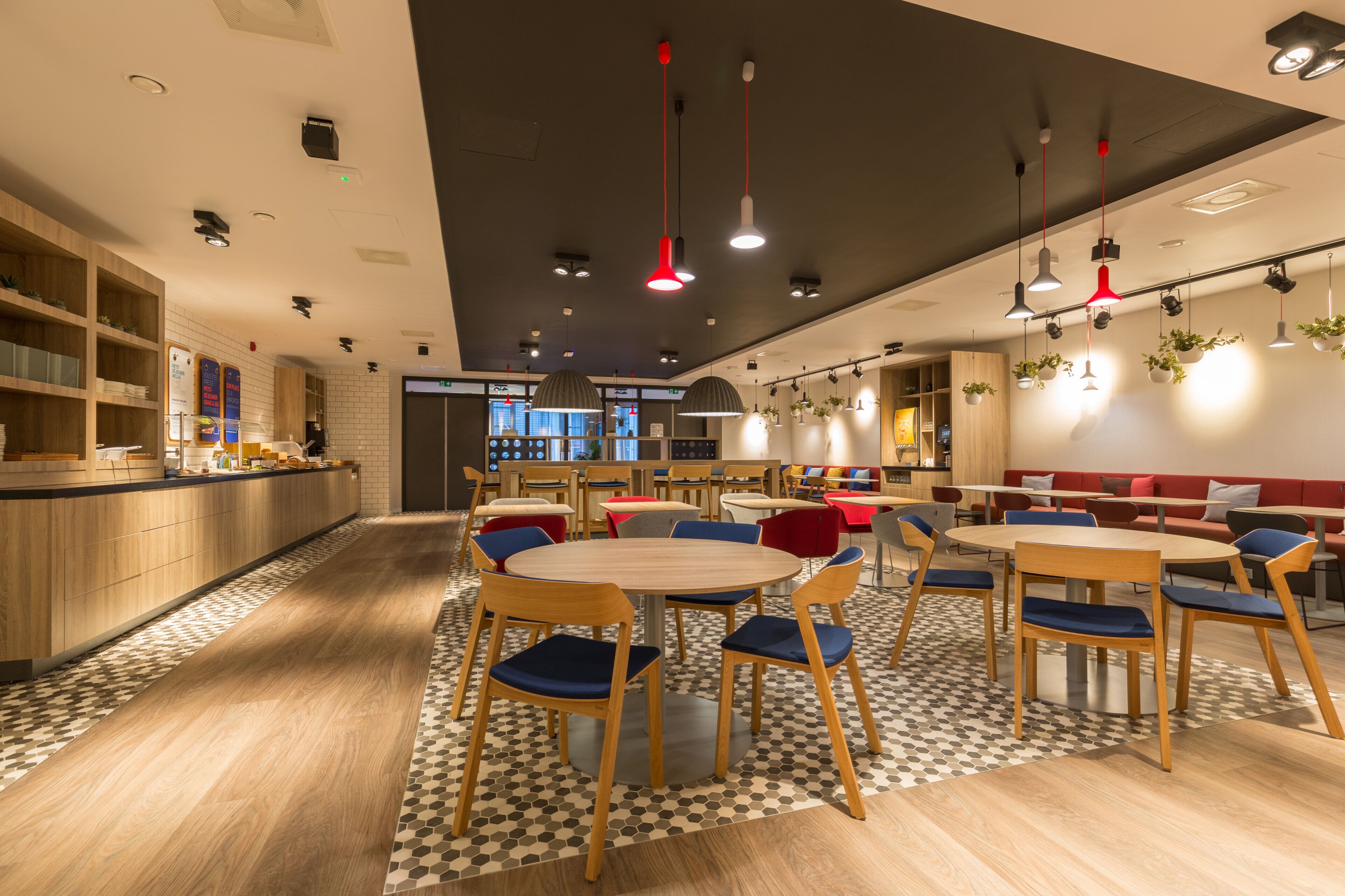 A modern restaurant with wooden tables and chairs, a check-in counter, and hanging plants.