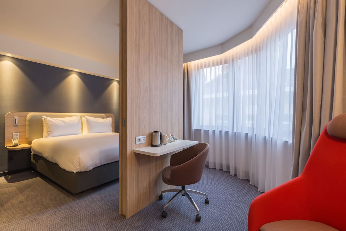 A hotel room with a bed, a desk, a chair, and a window with curtains.