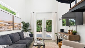 A modern living room with a grey sofa, a coffee table with books, a TV on the wall, and a large window with curtains. -  THE JACK 3 (Waco)