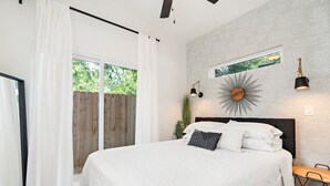 A bedroom with a large bed, white bedding, a sunburst wall decoration, and a window with a view of greenery. -  THE JACK 3 (Waco)