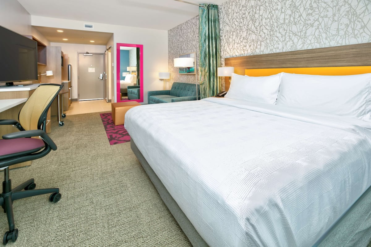 A hotel room with a large bed, a desk with a chair, a television, and a mirror.