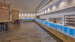 A modern breakfast area with a long counter, seating, and a coffee machine. - Home2 Suites by Hilton Wichita Falls, TX (Wichita Falls)