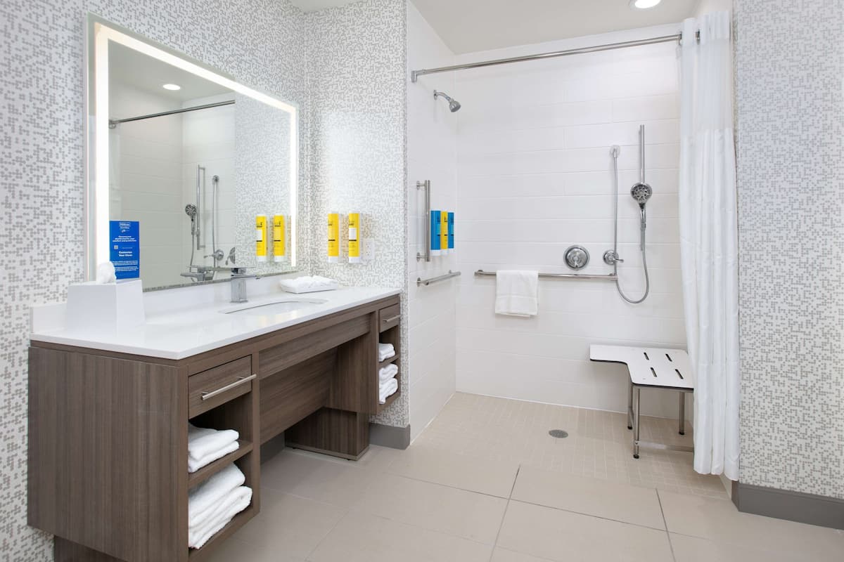 A modern bathroom with a large mirror, dual sinks, a shower, and a vanity with storage.