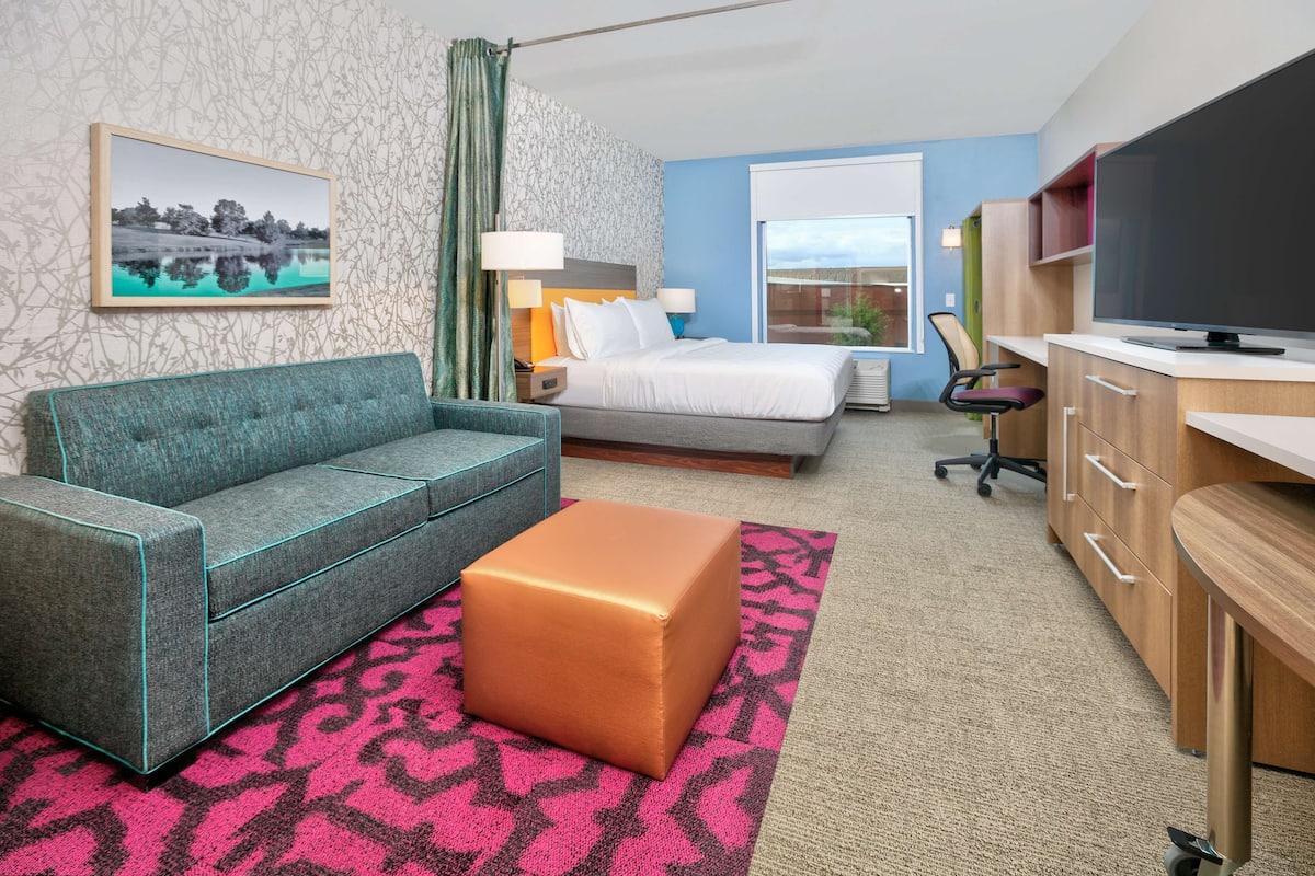 A hotel room with a bed, a sofa, a desk with a TV, and a window.